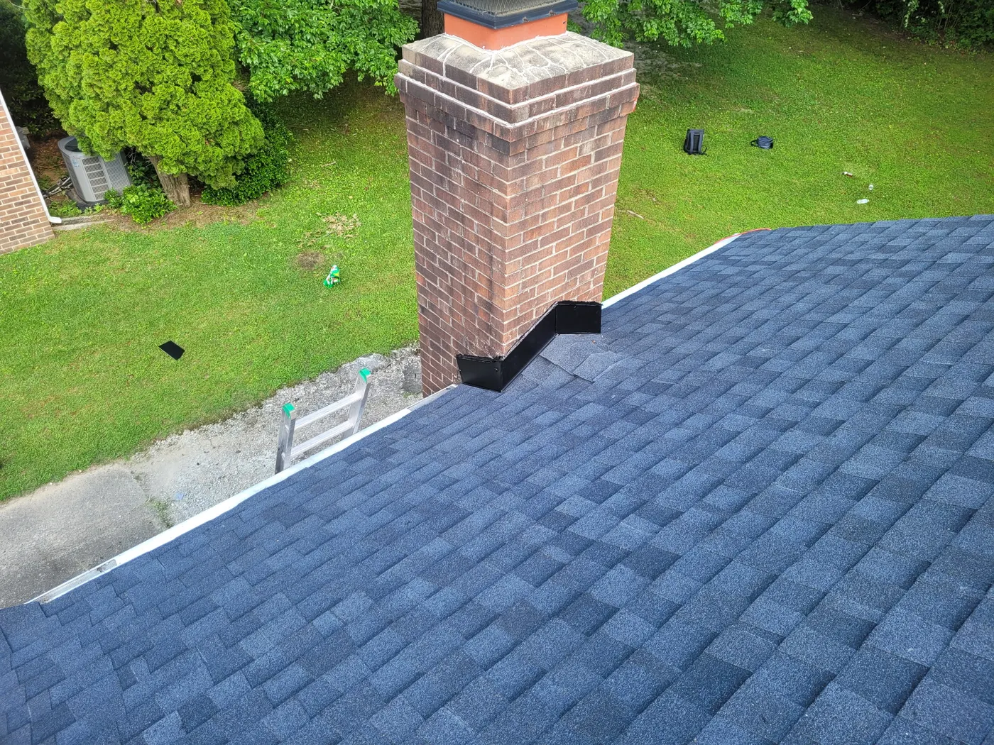 New black step flashing sealed around a brick chimney on fresh shingles